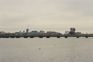 Charles River viewed toward Boston with the Harvard Bridge spanning the water, buoys floating in the foreground, skyline with the Citgo sign and stacked BU building under overcast sky